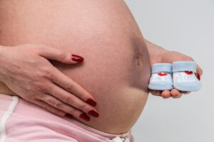trudnica u devetom mesecu trudnoce drzi decije cipelice u jednoj ruci spremna da se porodi carskim putem